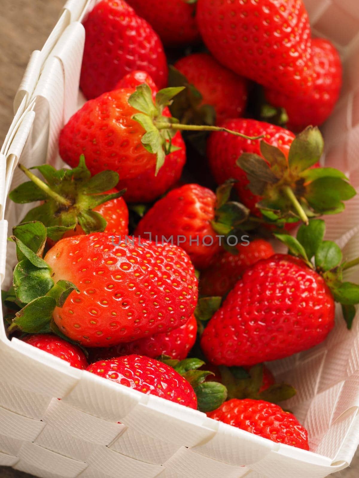 Fresh organic strawberries in a white basket on a rustic wooden table
