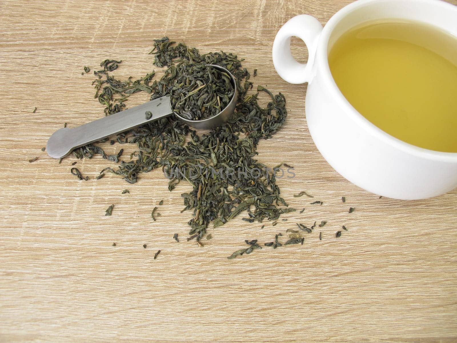 Green tea Chun Mee in tea measure and a cup of green tea