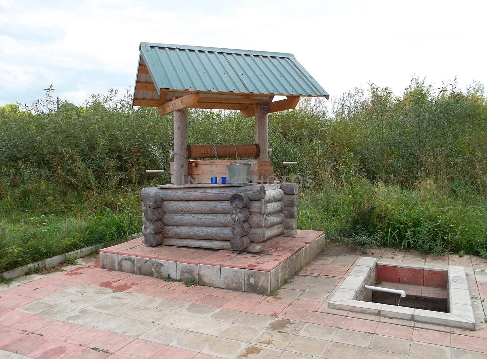 Well made of wooden logs in the Russian village amid tall grass.