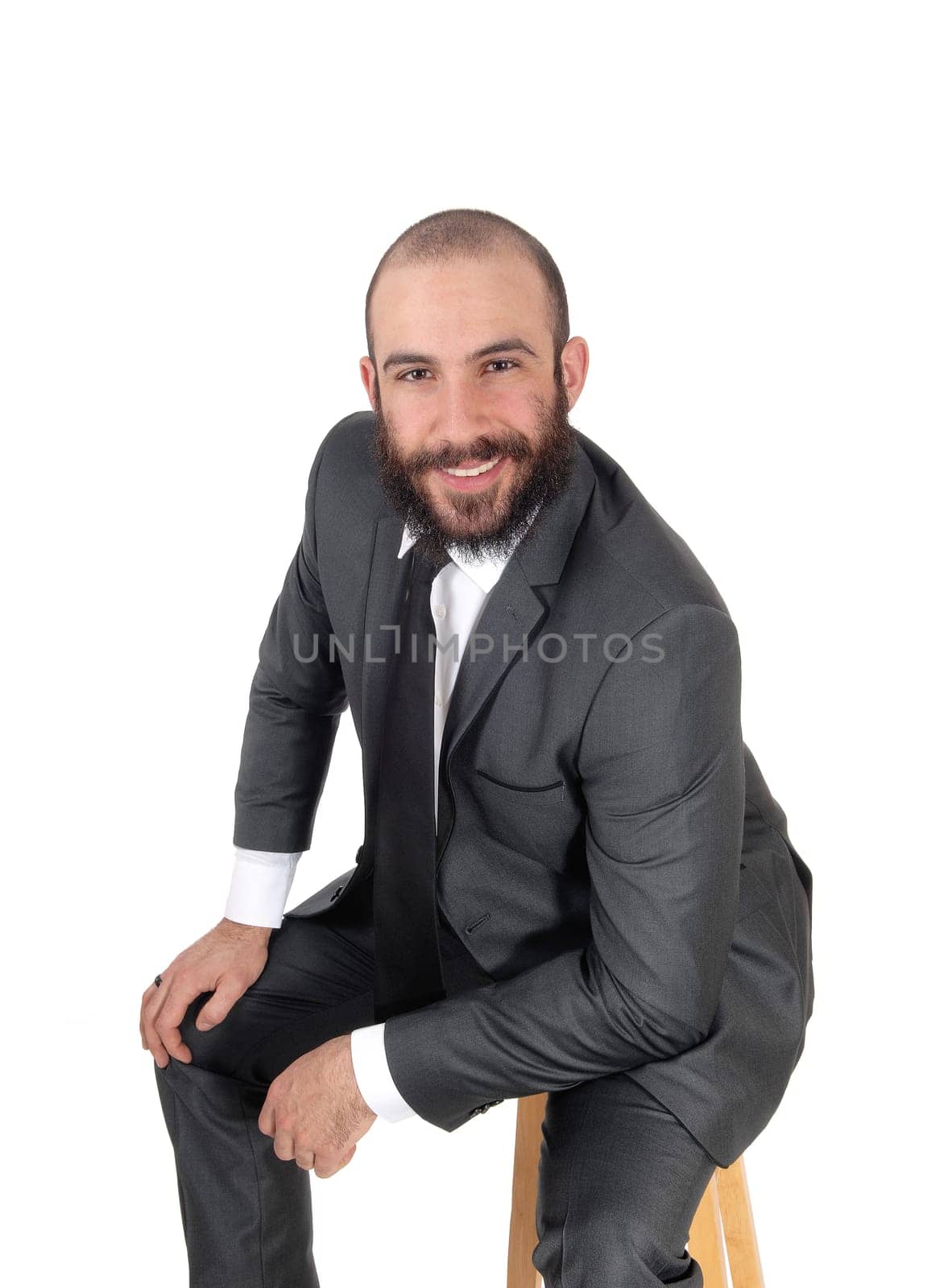 A young businessman sitting on a bar chair in a suit and .beard and mustache, smiling, isolated for white background.
