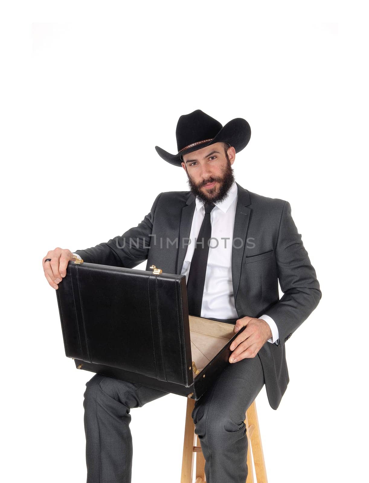 A handsome young business man sitting with his briefcase on his knees.wearing a black cowboy hat, isolated for white background.