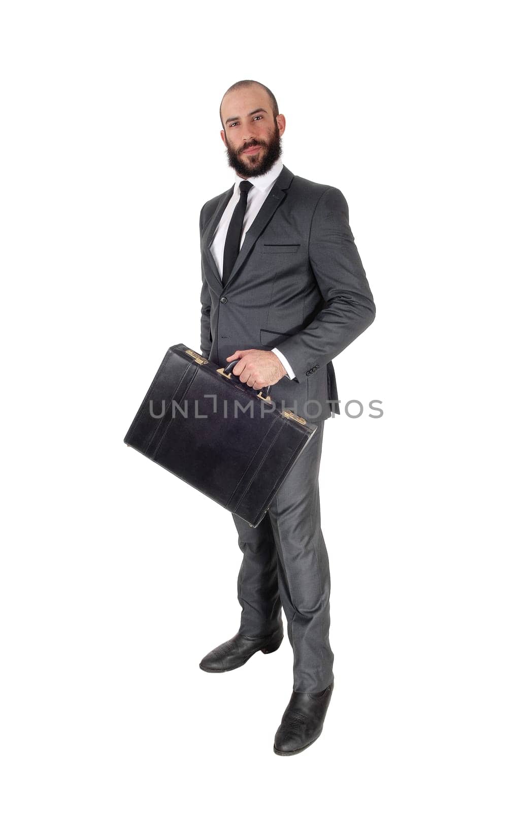A young handsome business man standing in profile and holding his.black briefcase, isolated over white background.
