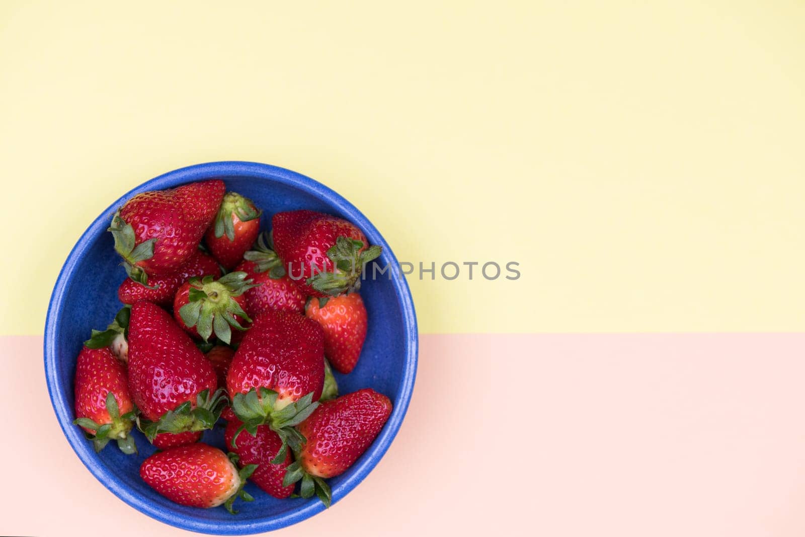 strawberries in blue bowl on pastel orange and yellow ground from above