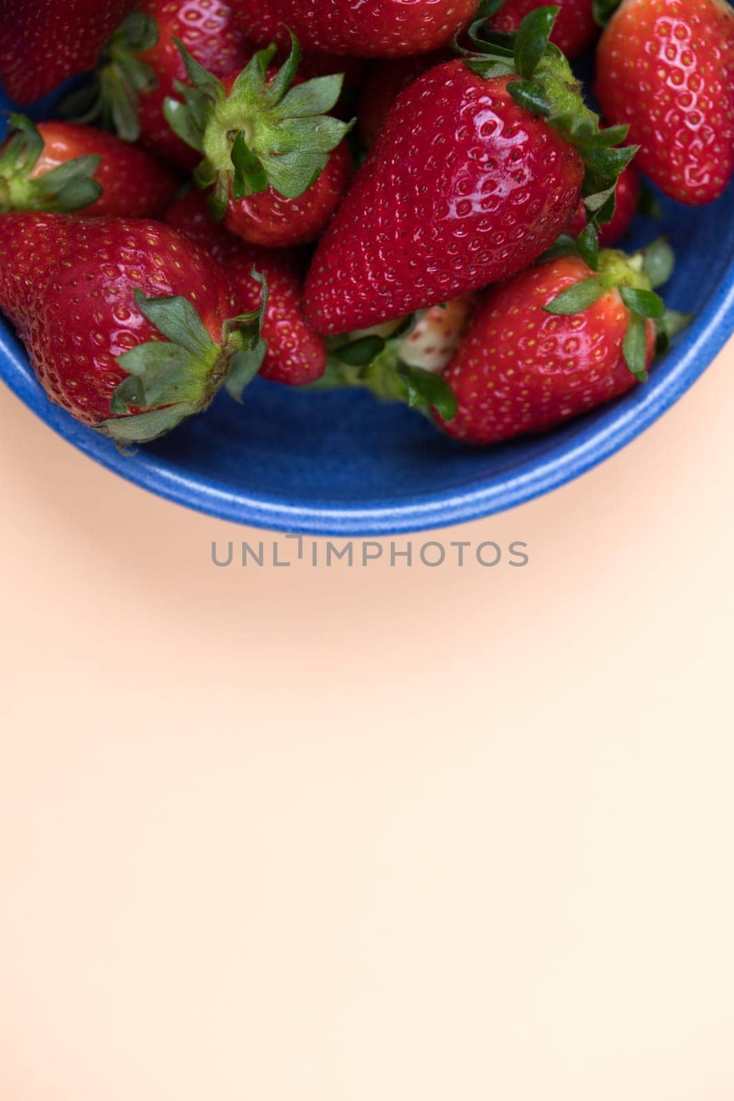 strawberries in blue bowl on pastel orange ground from above