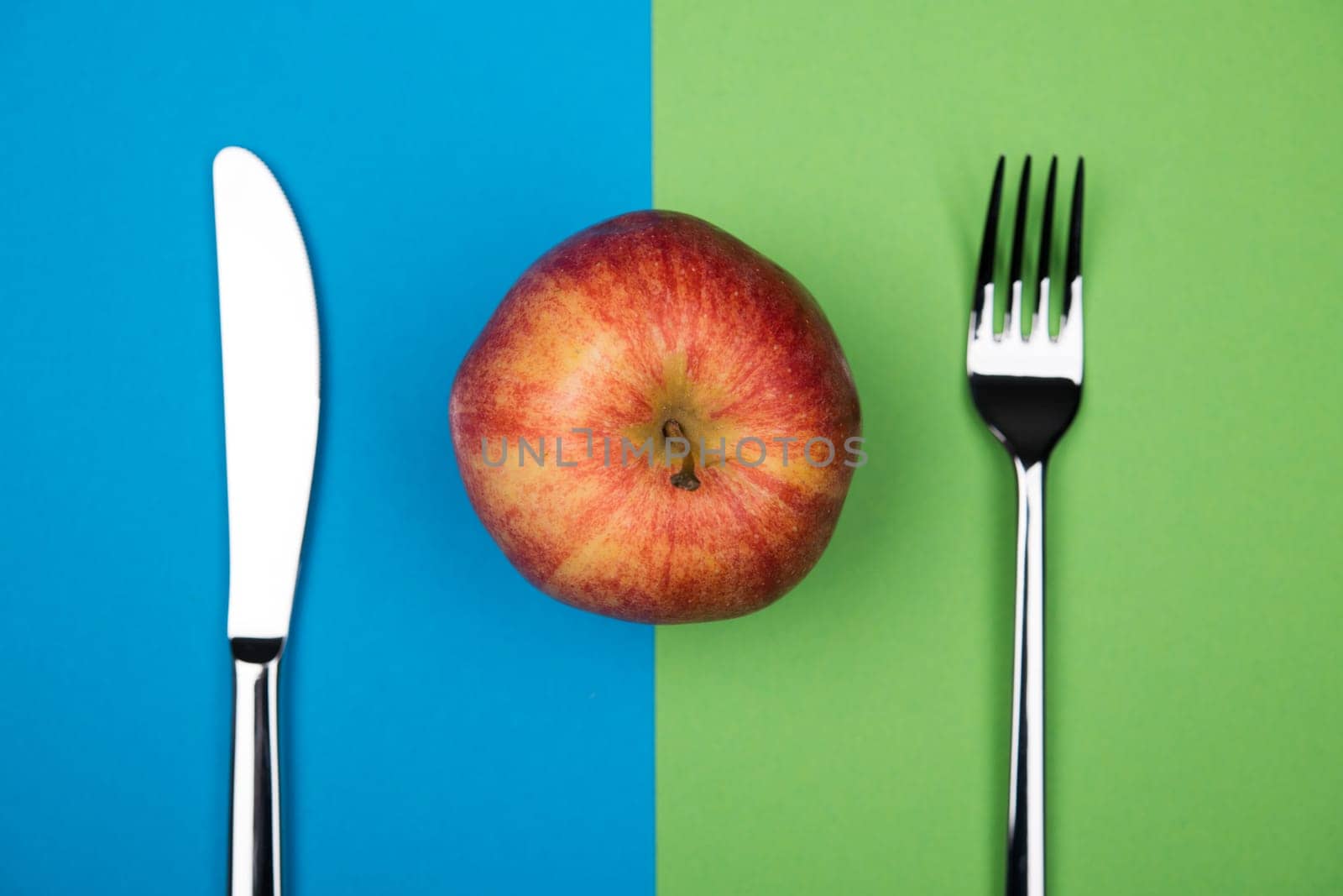 red apple from above with knife and fork on blue and green ground