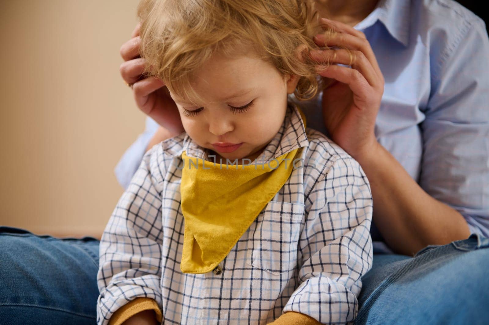 A loving mother adjusts her little son's outfit. The child sits peacefully, conveying warmth and affection. A tender moment reflecting love and family care.