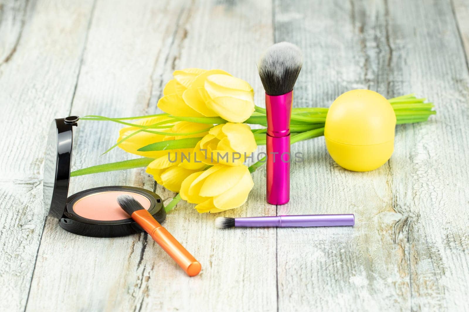 Decorative composition of various professional cosmetic brushes with a bouquet of yellow tulips. Presented on a rustic bright wooden table. Concept  greeting card design.