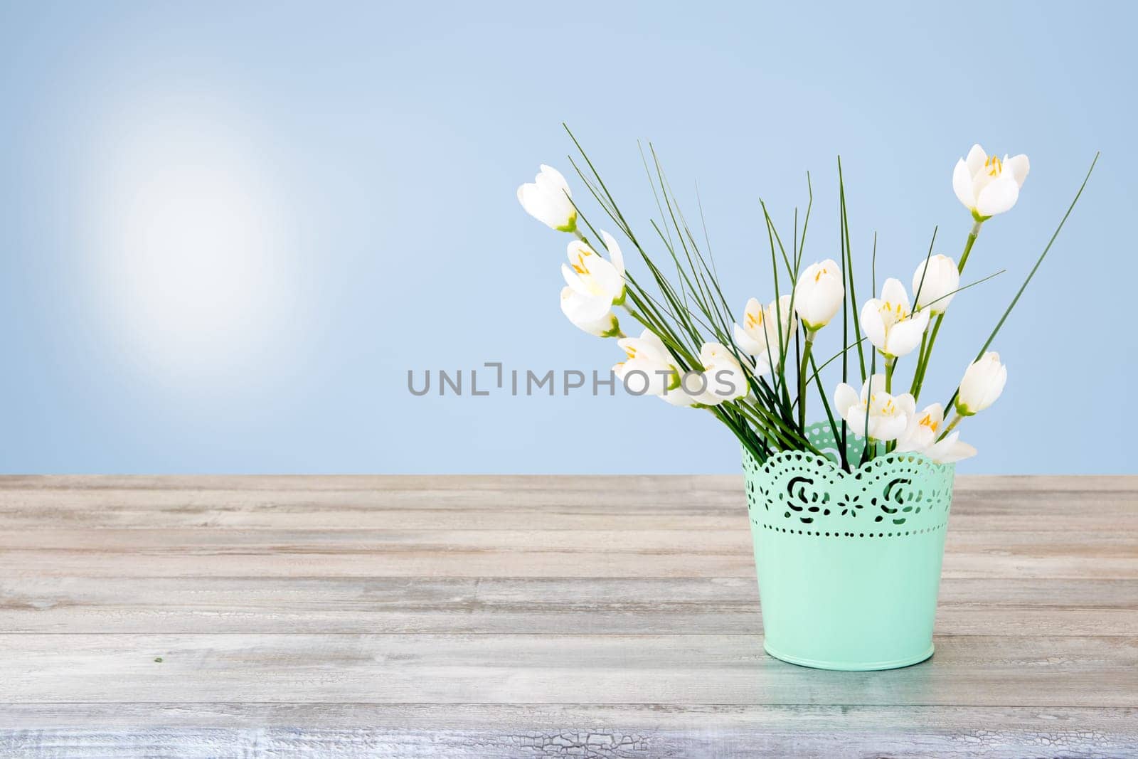 Decorative composition of white flowers Bouquet on rustic bright wooden table. Concept card. The natural bright background with sun is shining. The bunch of white flowers is in decorative green vase.  Empty space for your design. Card concept for mothers day, birthday, aniversary and other events.