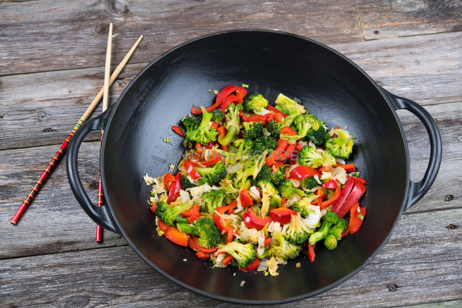 wok with colorful vegetables and chopsticks on wooden ground