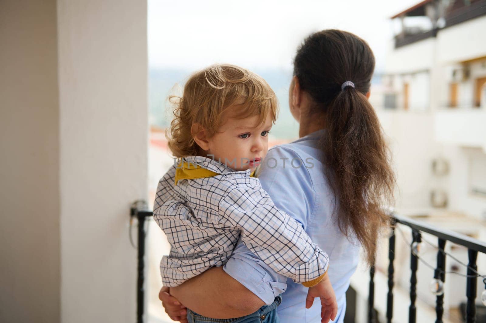 A loving mother holds her child while standing on a balcony, symbolizing warmth, care, and family togetherness in an urban setting.