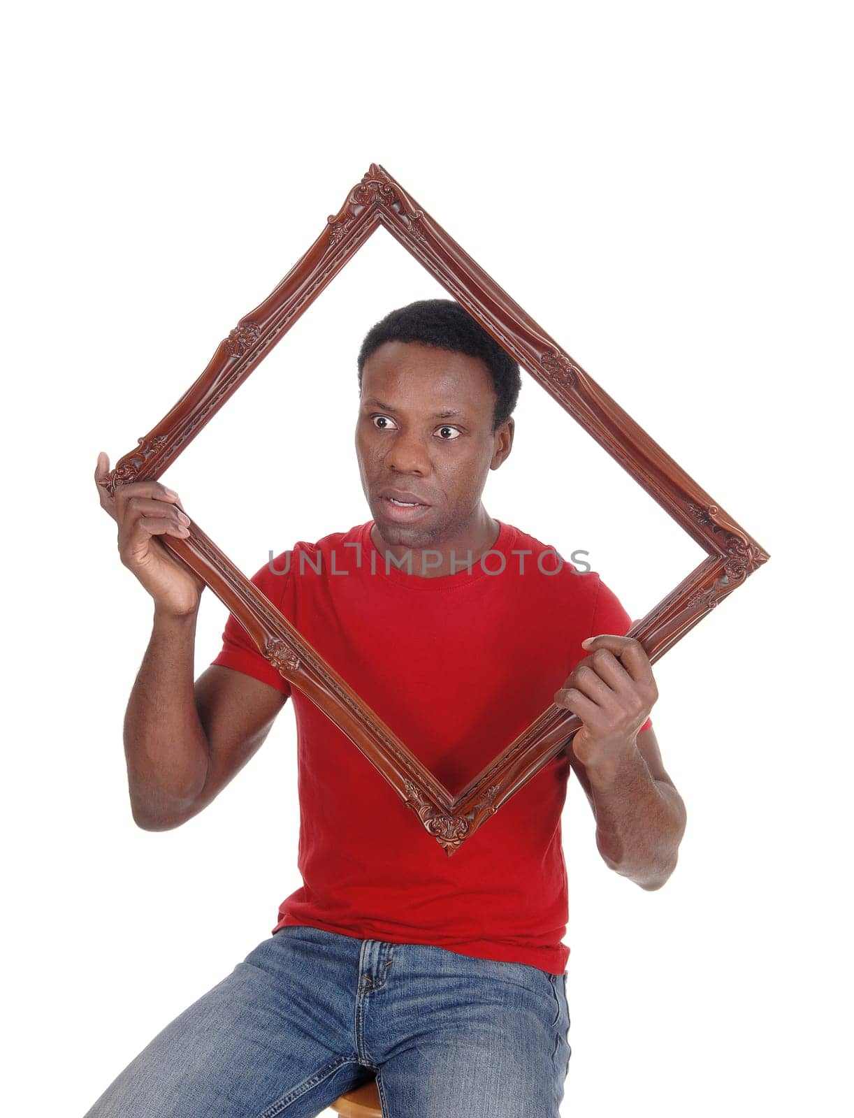 Scared looking African American man holding up a picture frame.in a red t-shirt, isolated for white background.
