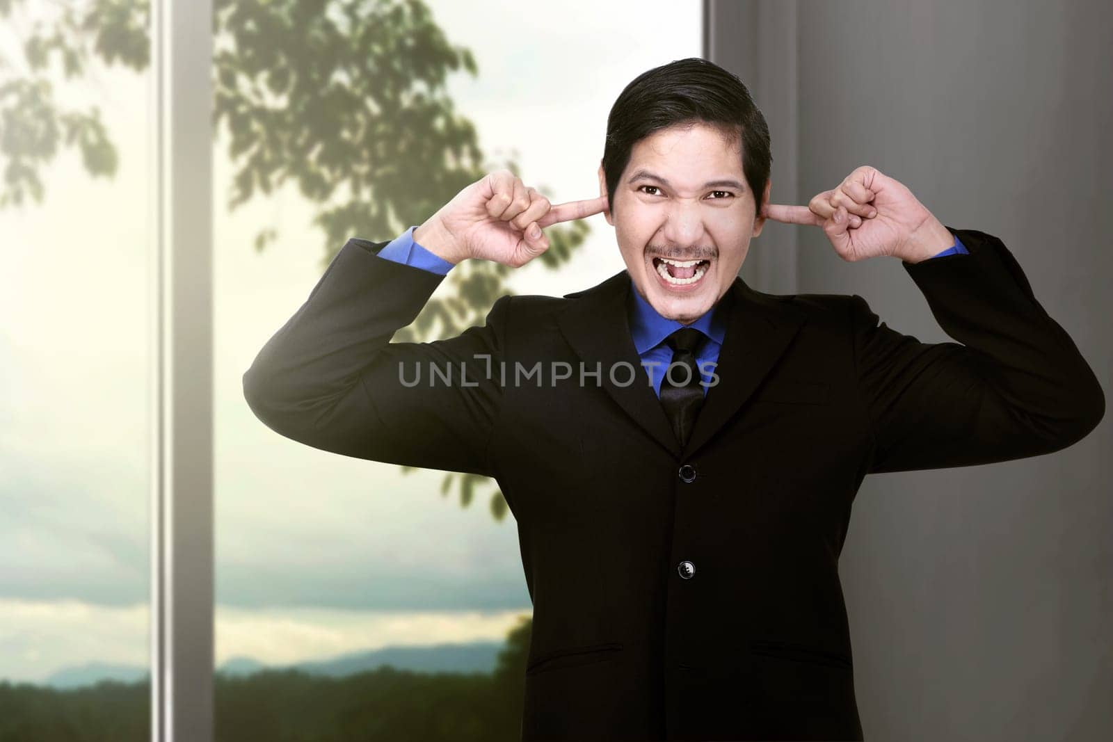 Unhappy asian businessman covering his ears to not hear great noise at home