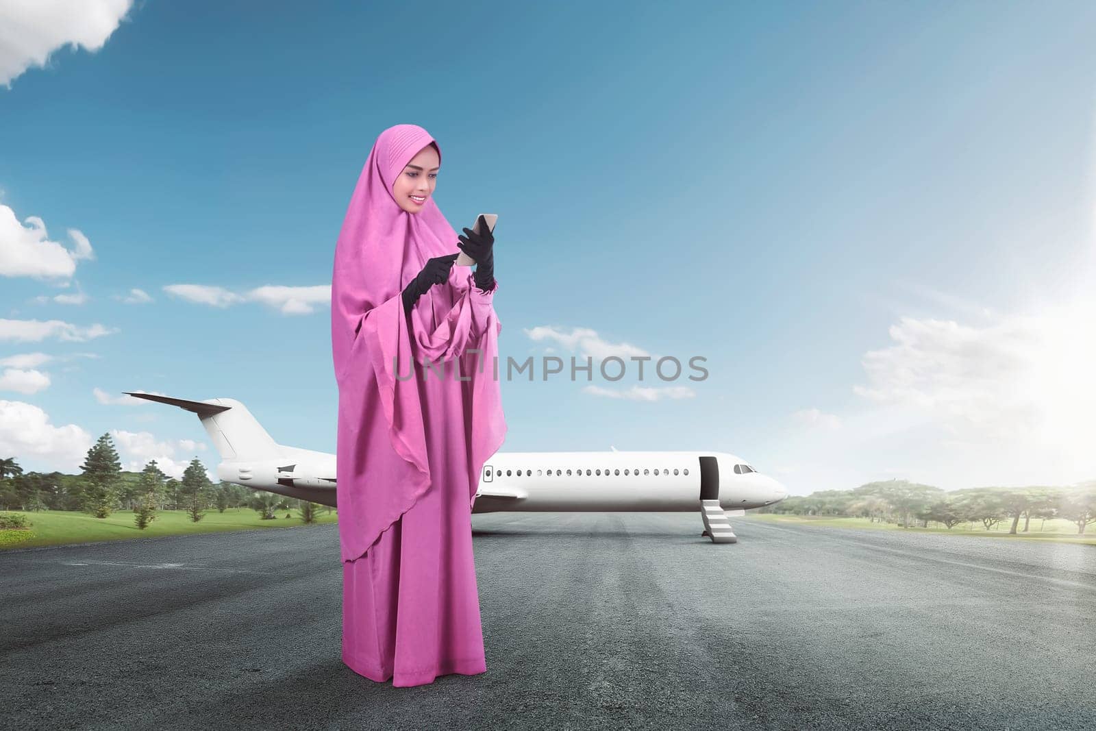 Happy asian female muslim with smartphone standing at outdoor