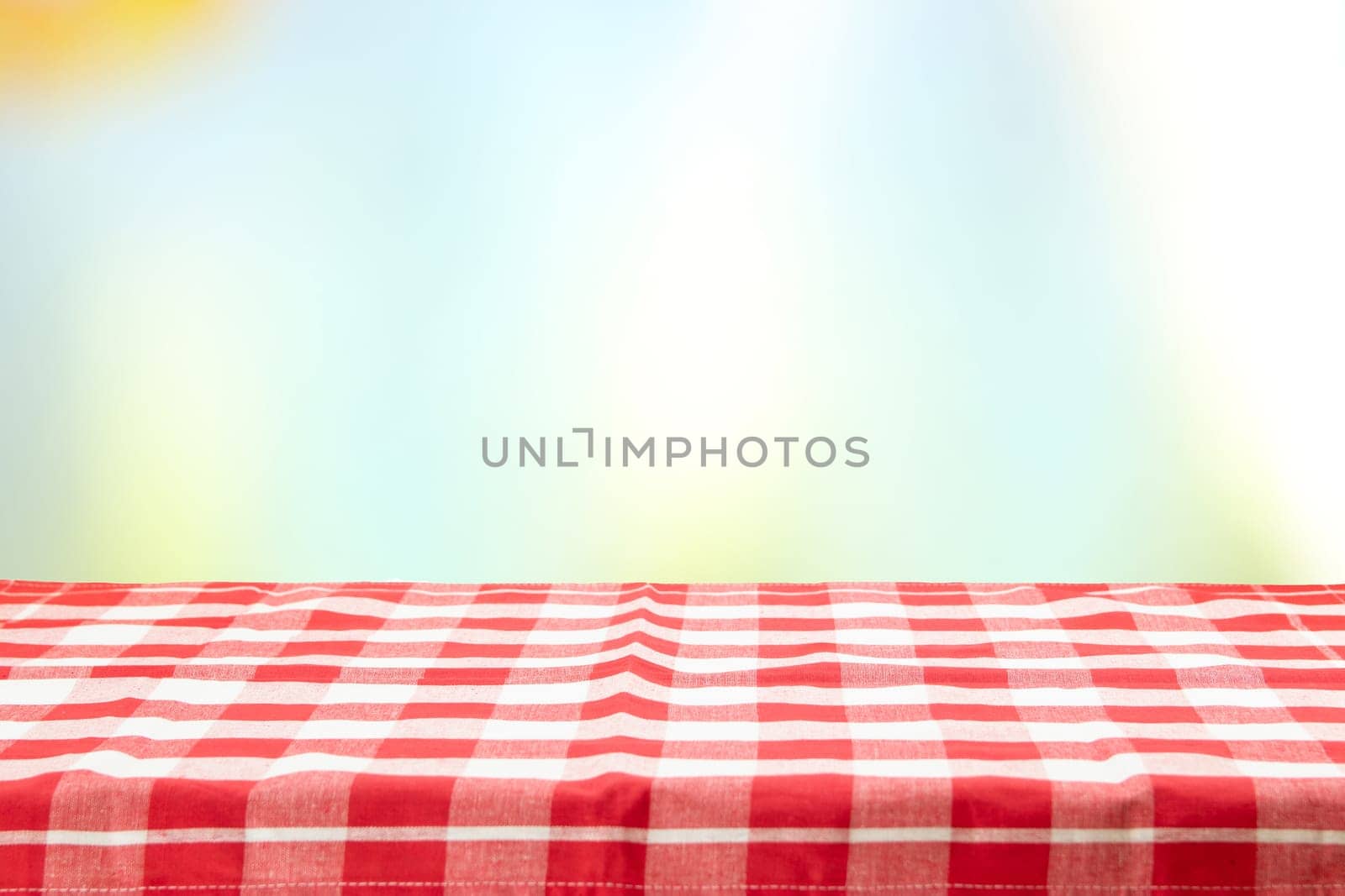 An empty table with a red checkered tablecloth and an pastel colorful natural background on a  sunny day. For your food and product display montage. Concept food.