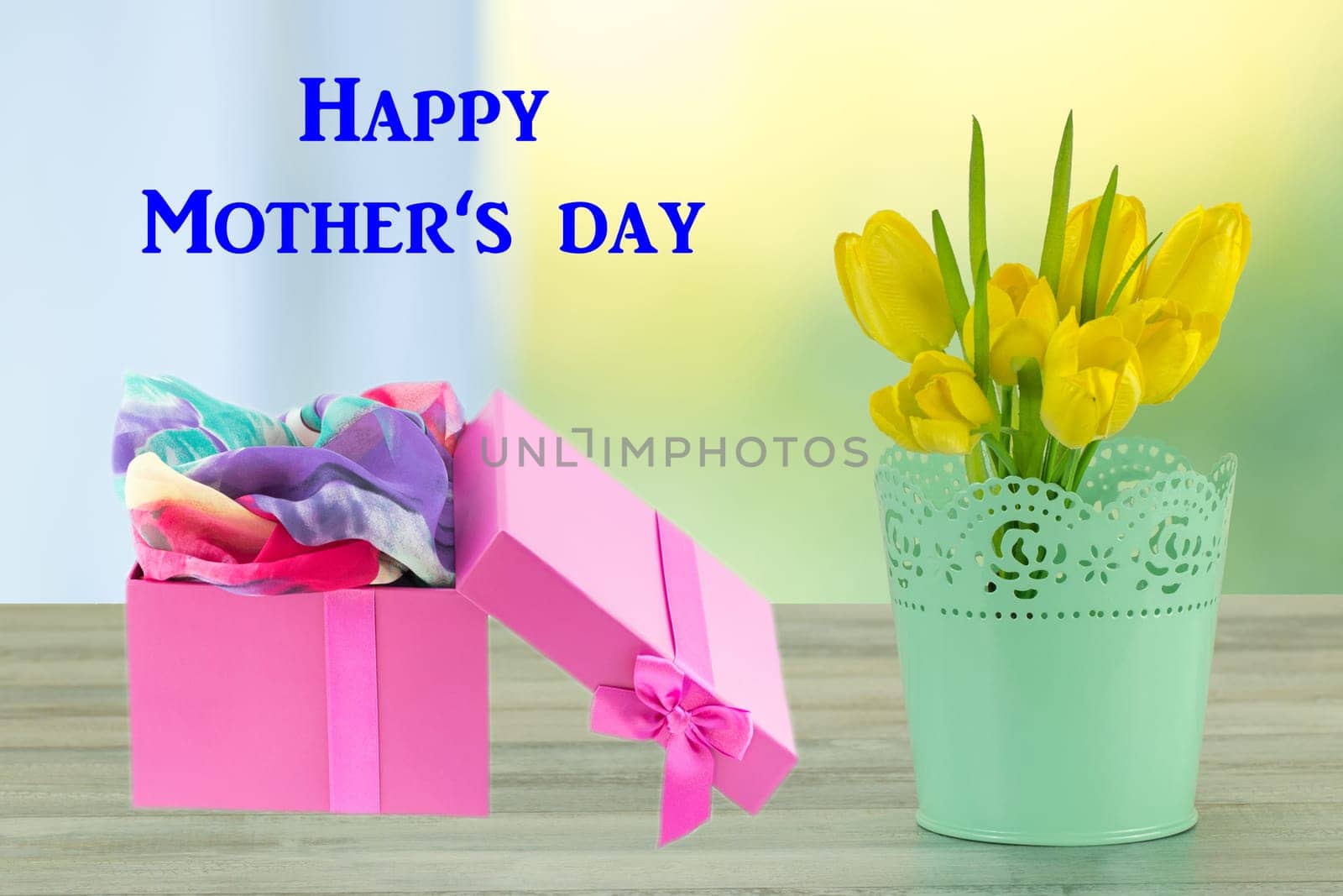 Mothers day greeting card. Decorative composition of yellow tulips on rustic bright wooden table and gift box. The bunch of yellow tulips is in decorative green vase.