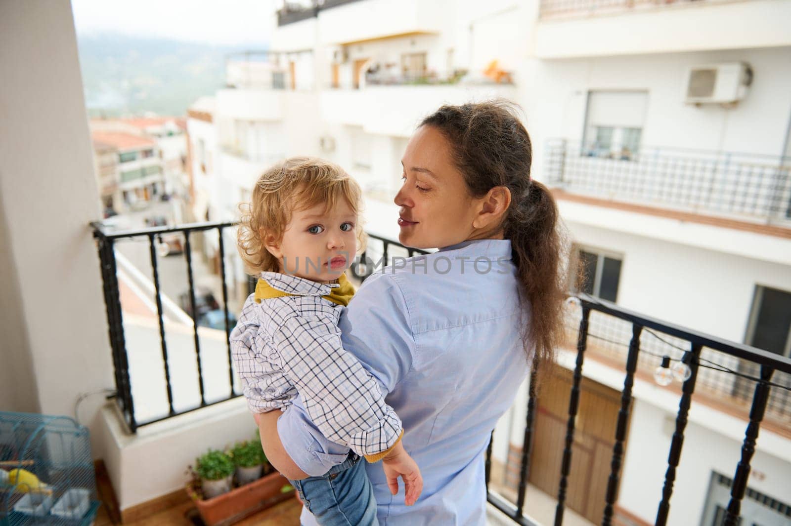 A mother joyfully spends time with her child on a balcony overlooking city buildings, embodying the love and connection shared between family members in a serene urban setting.