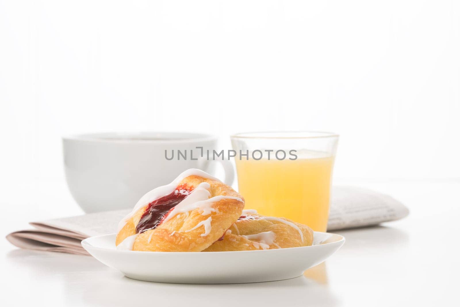 Fresh raspberry danish with coffee and a newspaper in the background.