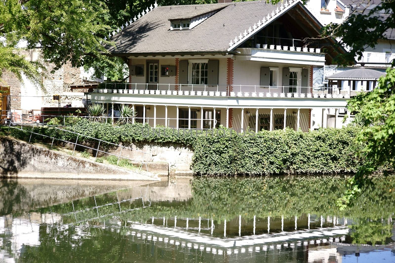 A residential building with a terrace is reflected on the banks of a river in the water.