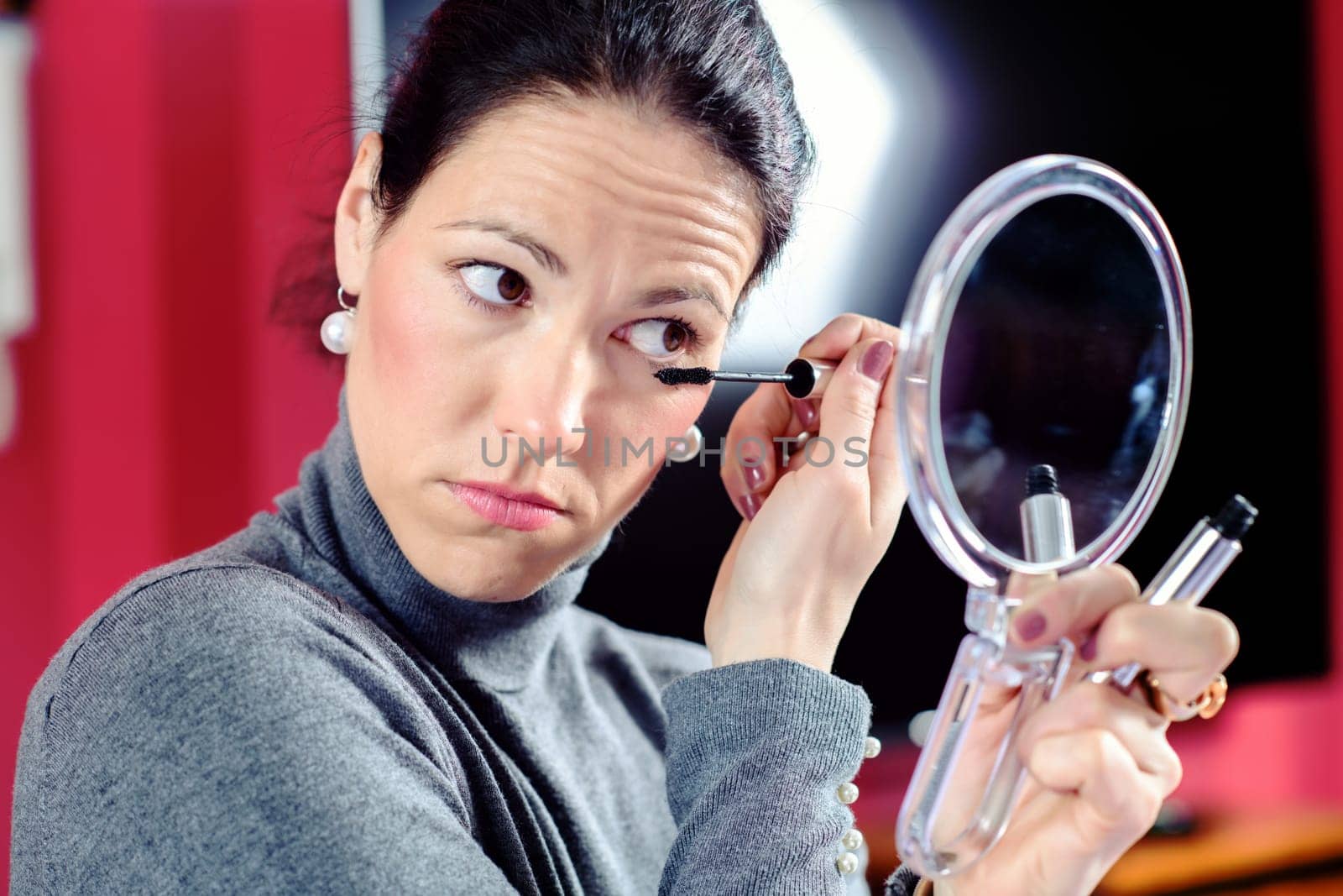 young dark haired woman looking in mirror and applying make up