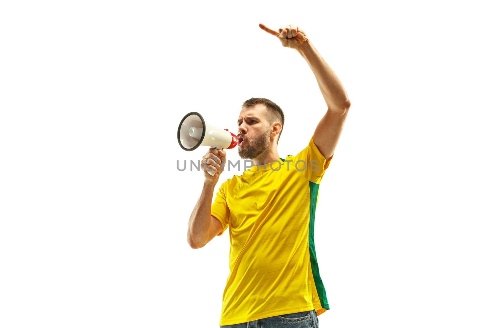 Brazilian fan celebrating on white background. The young man in soccer football uniform with megaphone at white studio. Fan, support, win, winner concept. Human emotions concepts.