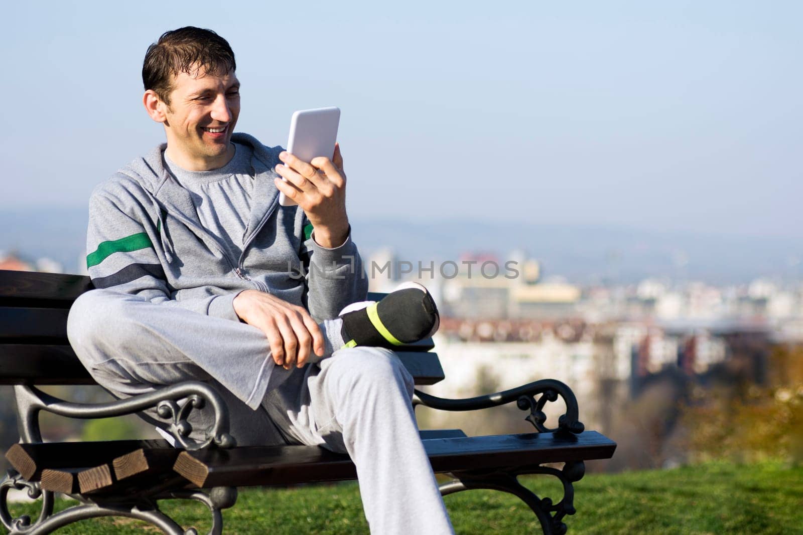 The smiling man is enjoying and using digital tablet outdoors on the bench.