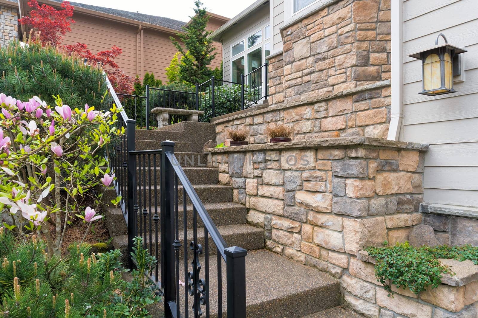 House front entry with concrete stairs iron rod railings stone wall planter siding by frontyard garden