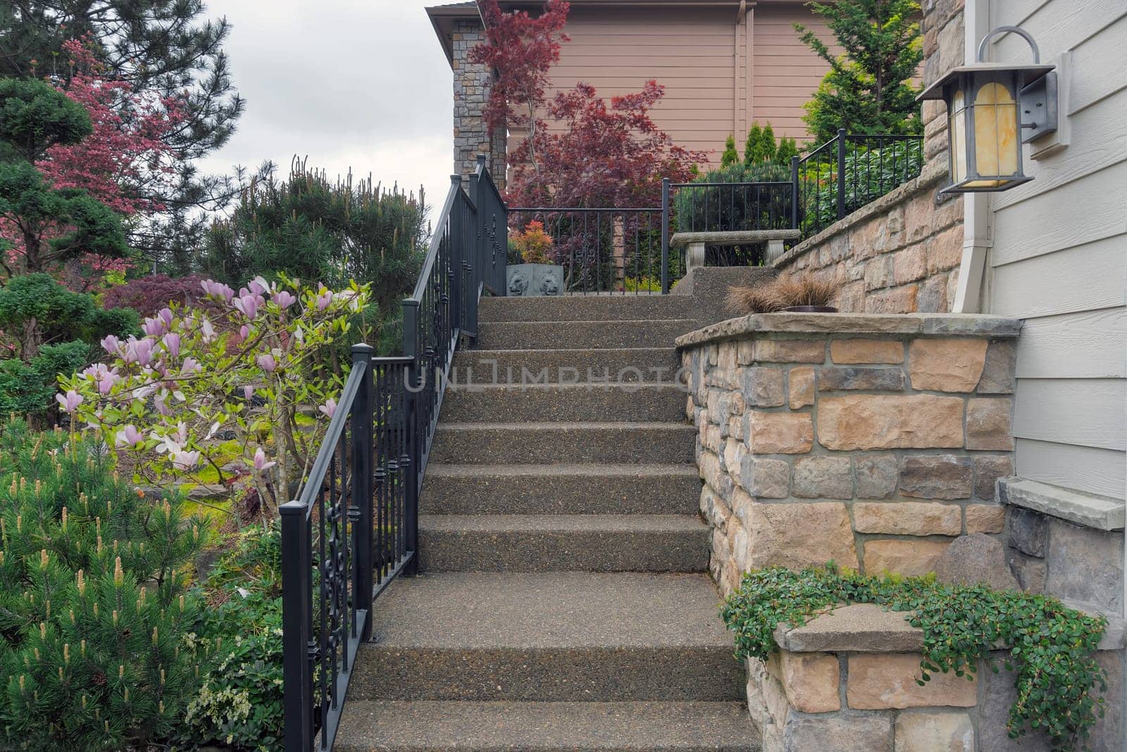 Concrete stair steps with railings and stone wall planters by frontyard garden to house door entrance