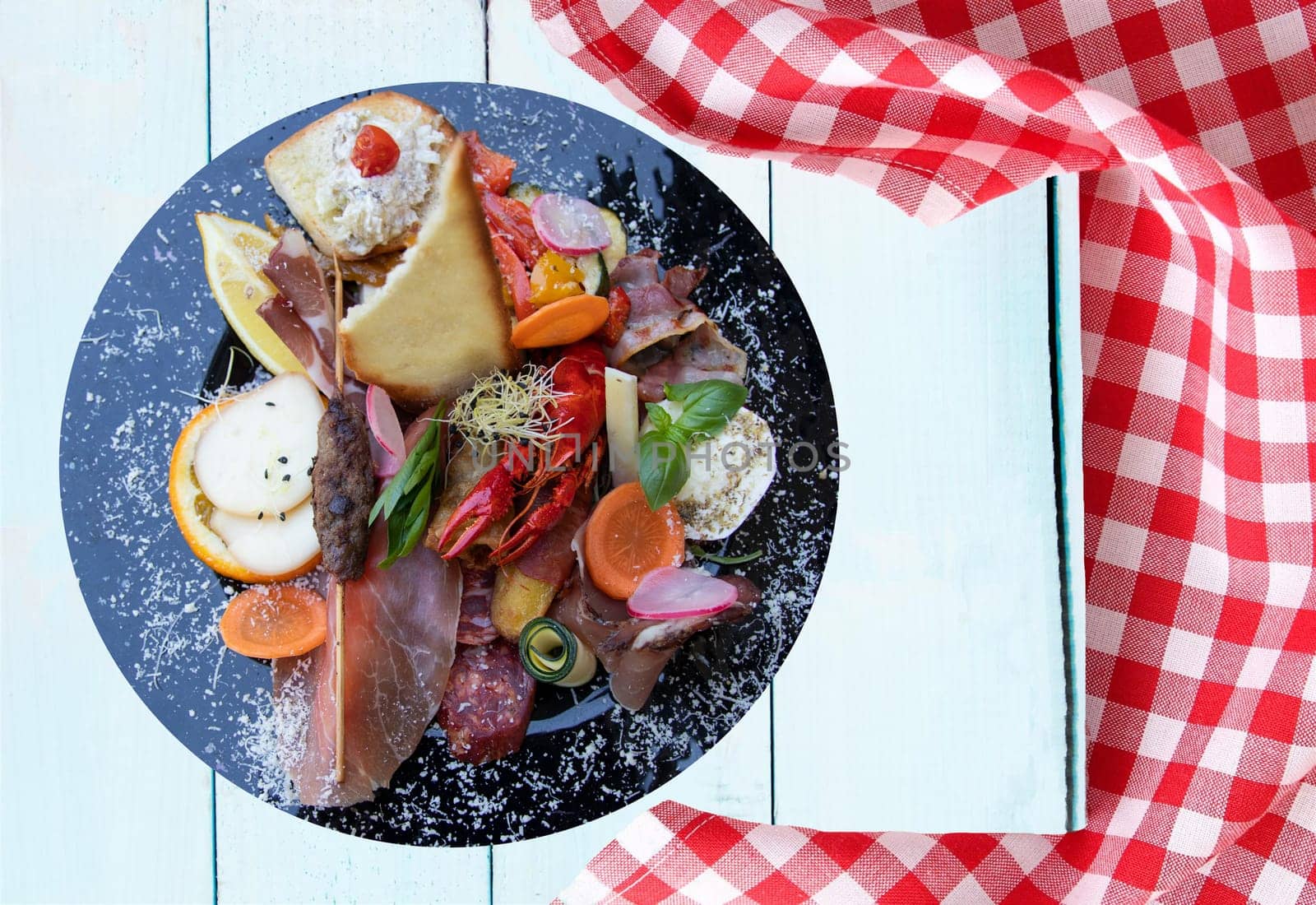Mixed typical Italian antipasto with ham vegetables and cancer. Concept traditional Italian food. Presented on rustic wooden bright table with red checkered tablecloth.