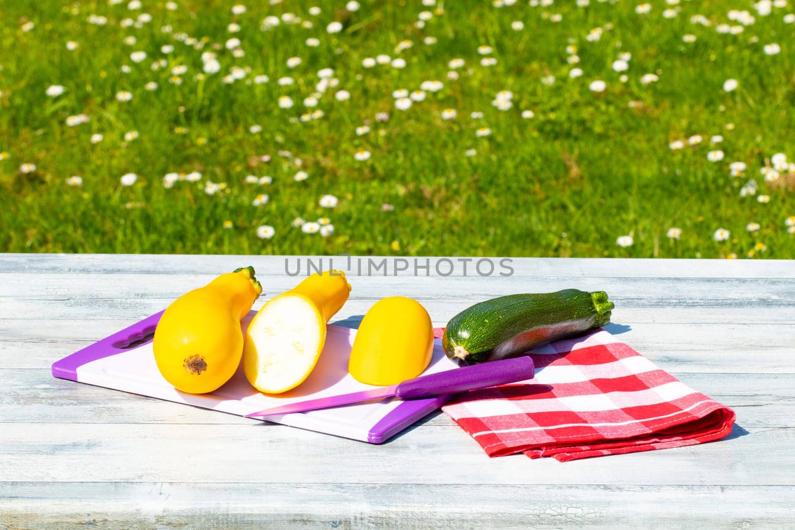 Three fresh courgette on rustic bright wooden table with natural green background. One of the yellow zucchini was freshly sliced on an cutting board. Concept health.