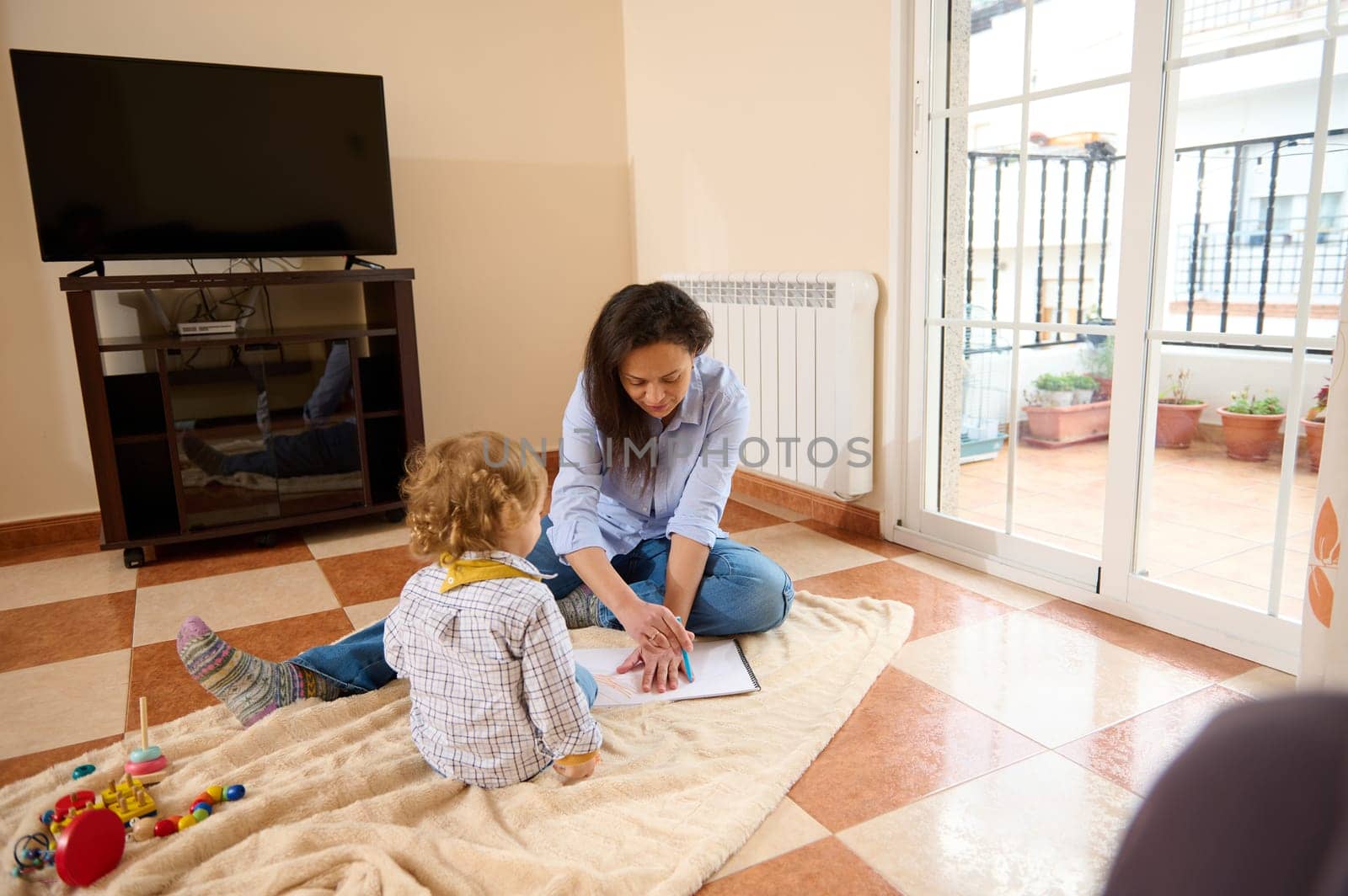 A loving mother spends quality time teaching her young child, fostering learning and bonding on a cozy blanket in a bright and warm home setting.