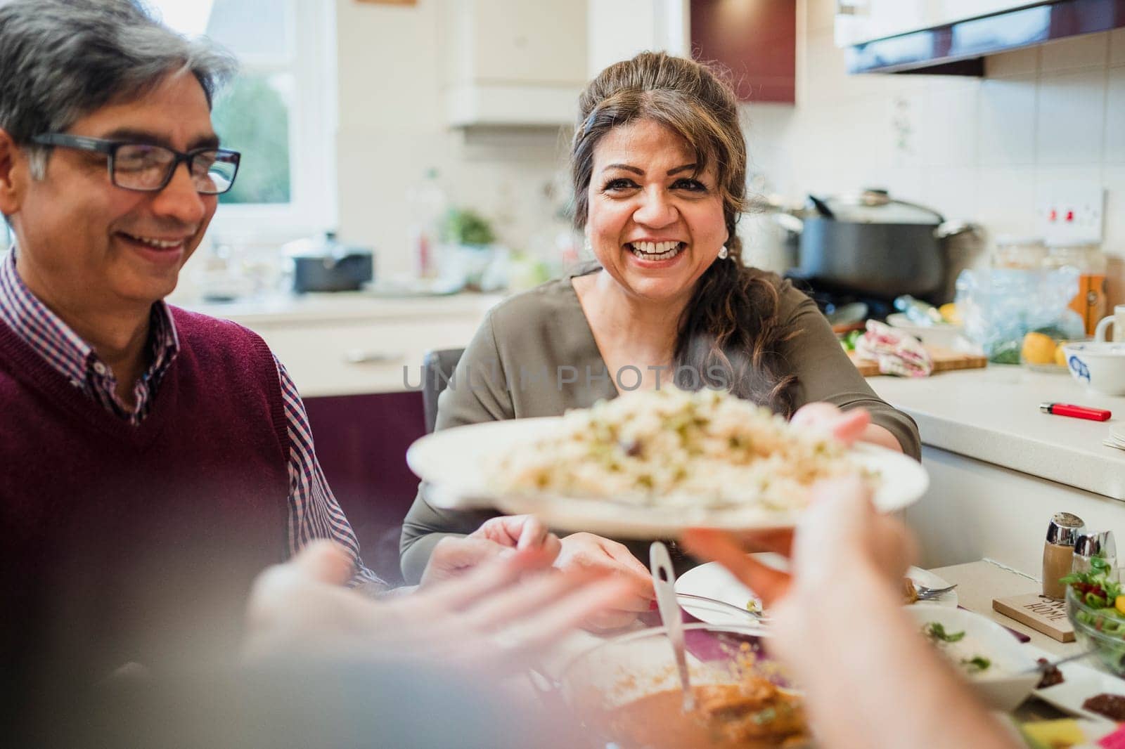 Point of view shot of a mature mother passing a serving of curry and rice to her son at the dining table.
