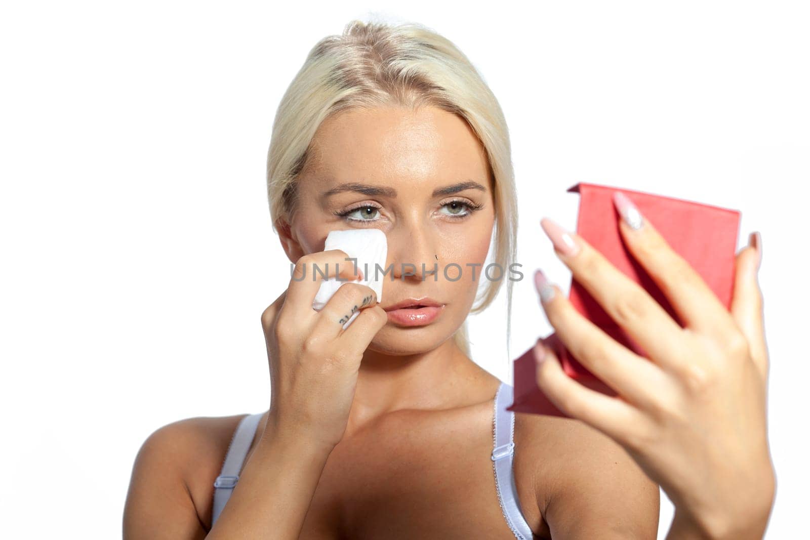 Young woman clean face and eyes with wet wipes, holding mirror, remove make-up, body breast lingerie