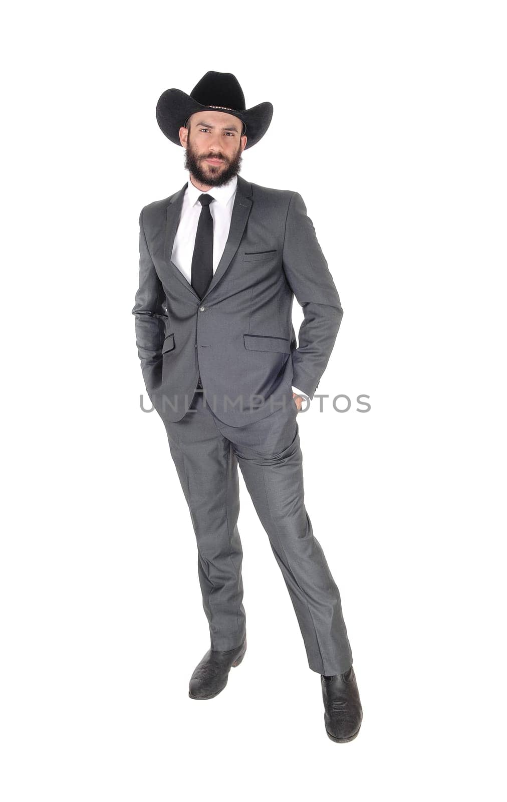 A handsome man standing in a gray suit and cowboy hat with his hands.in his pocket, with beard and mustache, isolated for white background.