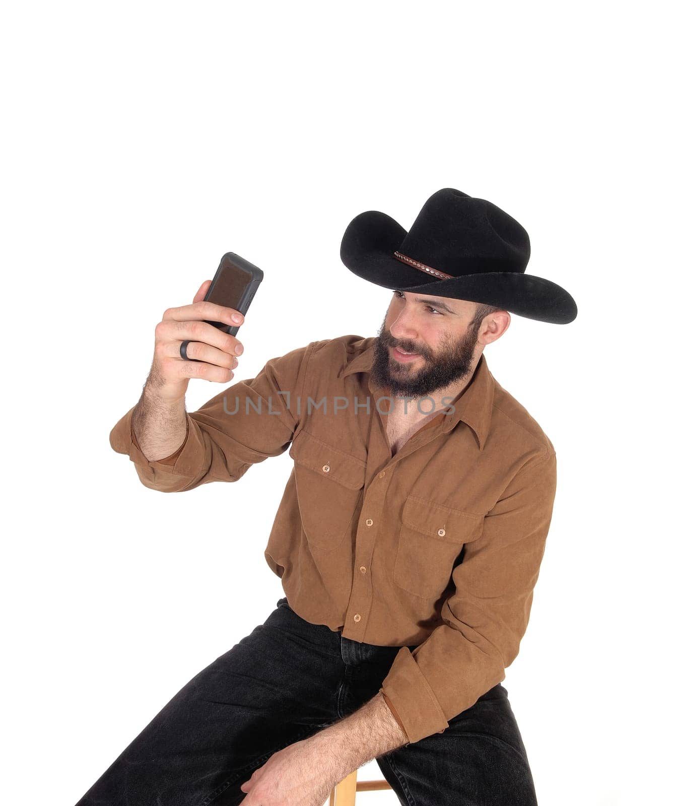 A young handsome man wearing a black cowboy hat and brown shirt.taking a selfie with his cell phone, isolated for white background.