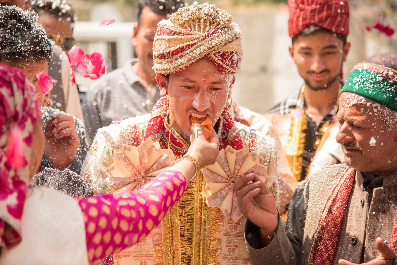 Shimla, India – April 19, 2017: Bride’s family feed sweet to groom as his relatives, friends and family look on during a welcome ceremony of traditional Indian wedding on April 19, 2017 in Shimla, Himachal Pradesh, India.