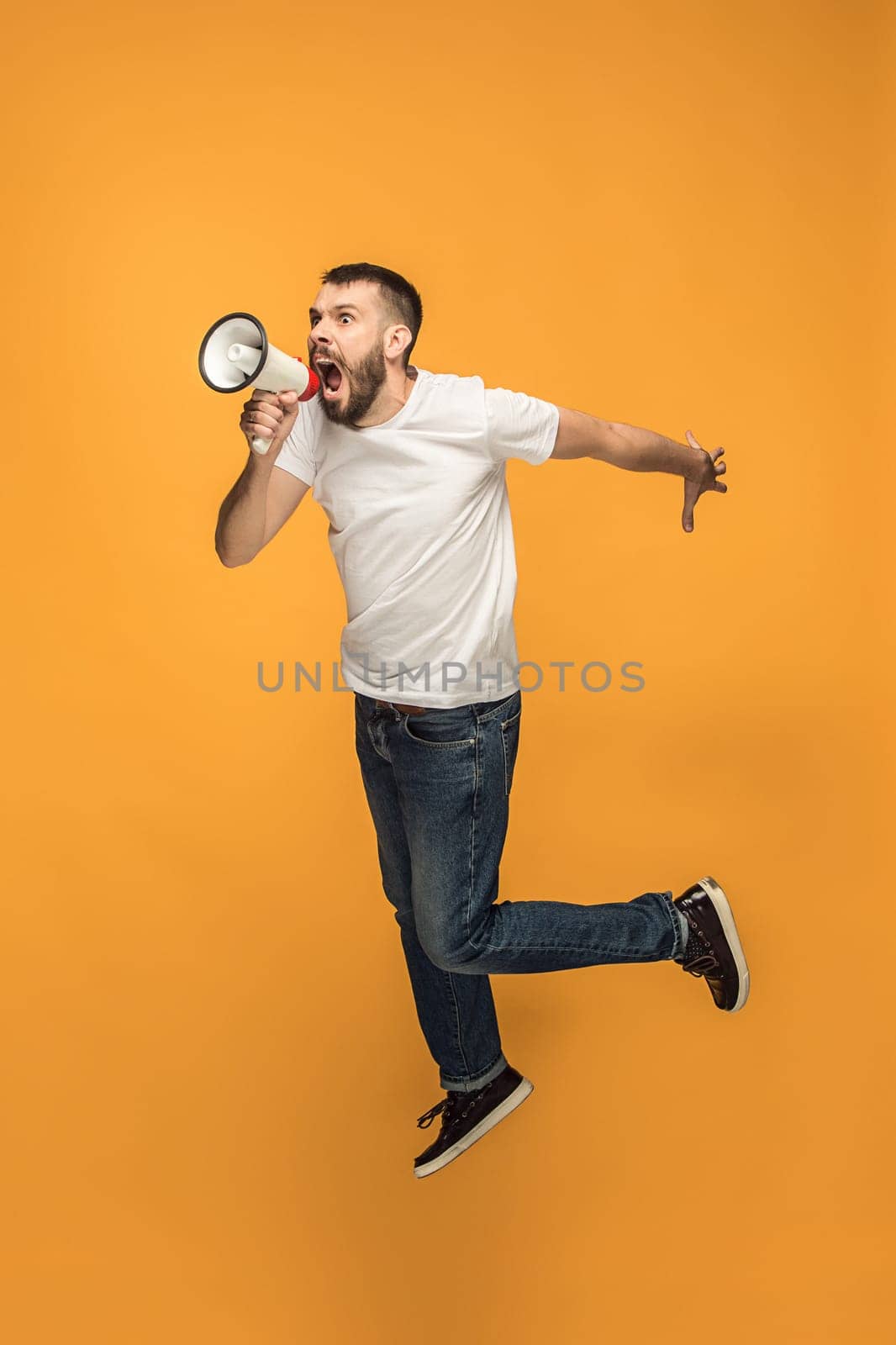 Soccer fan jumping on orange background. The young man as football fan with megaphone isolated on orange studio. Support concept. Human emotions, facial expression concepts.