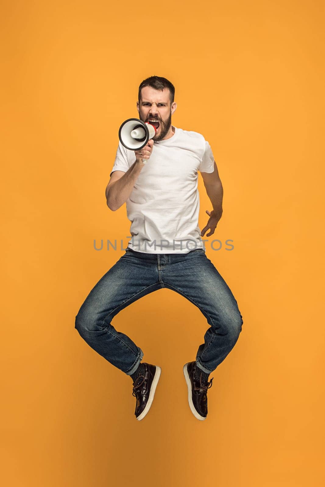 Soccer fan jumping on orange background. The young man as football fan with megaphone isolated on orange studio. Support concept. Human emotions, facial expression concepts.
