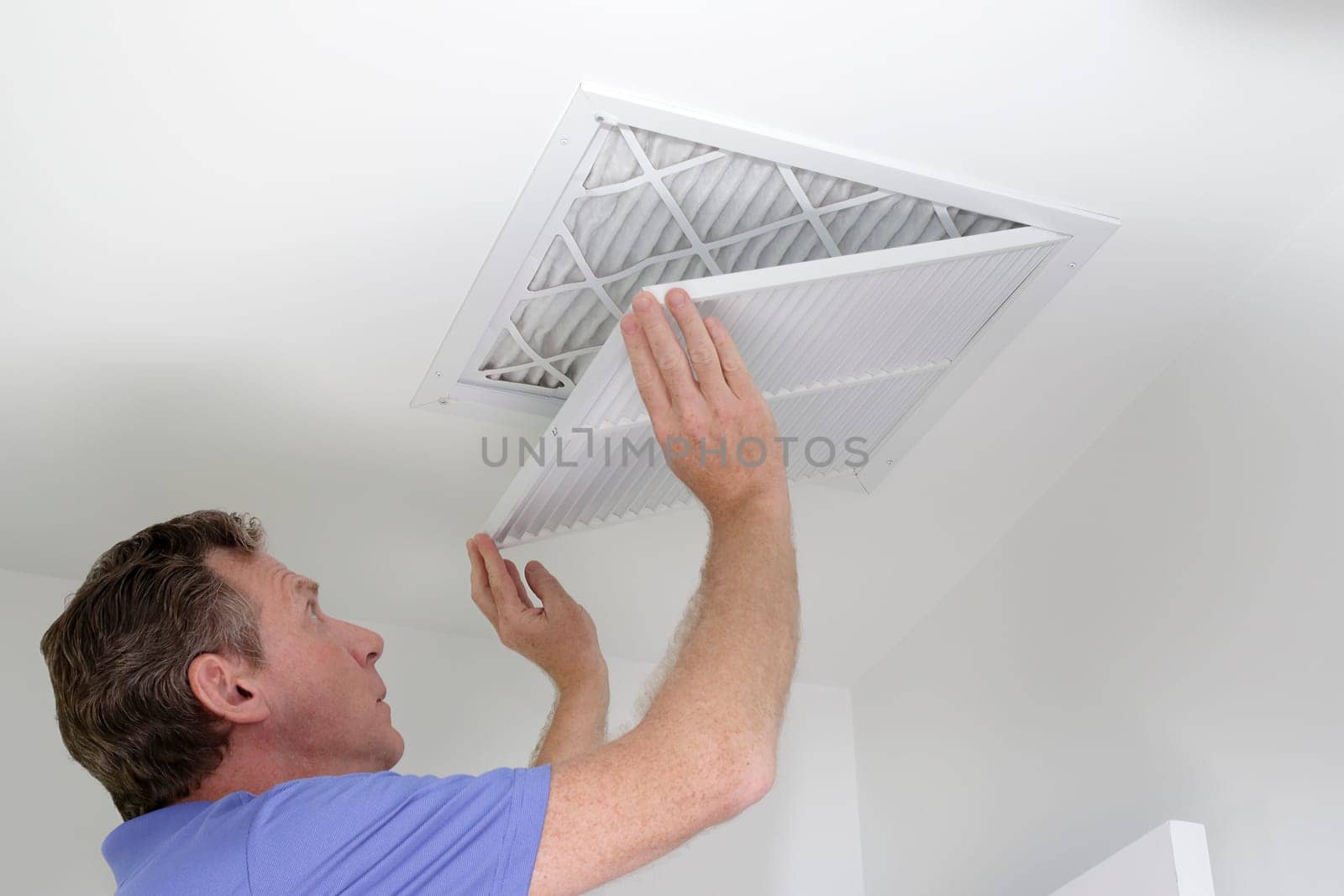 Man shutting grill of HVAC, heating ventilating and cooling after replacing the air filter. Closing ceiling grill after replacing an air filter in the ceiling.