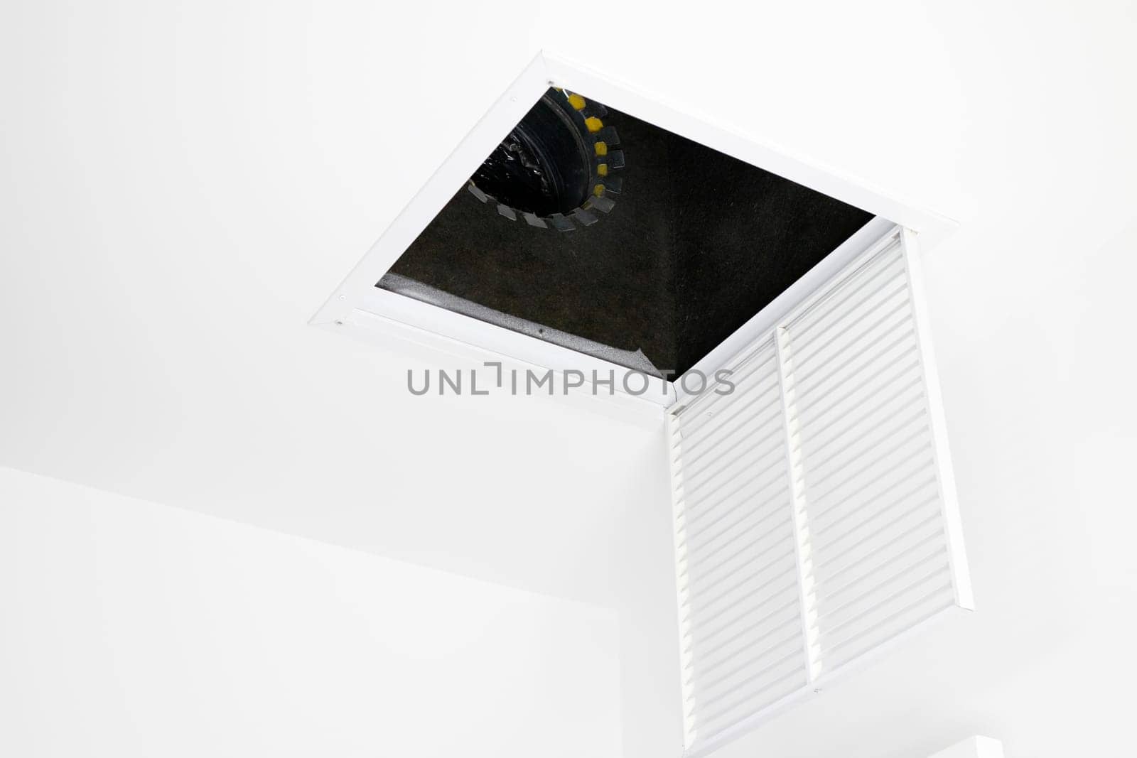 White square ceiling furnace air vent grate open, showing inside the duct. Metal air intake grate open and hanging from the ceiling showing view of inside the HVAC system.