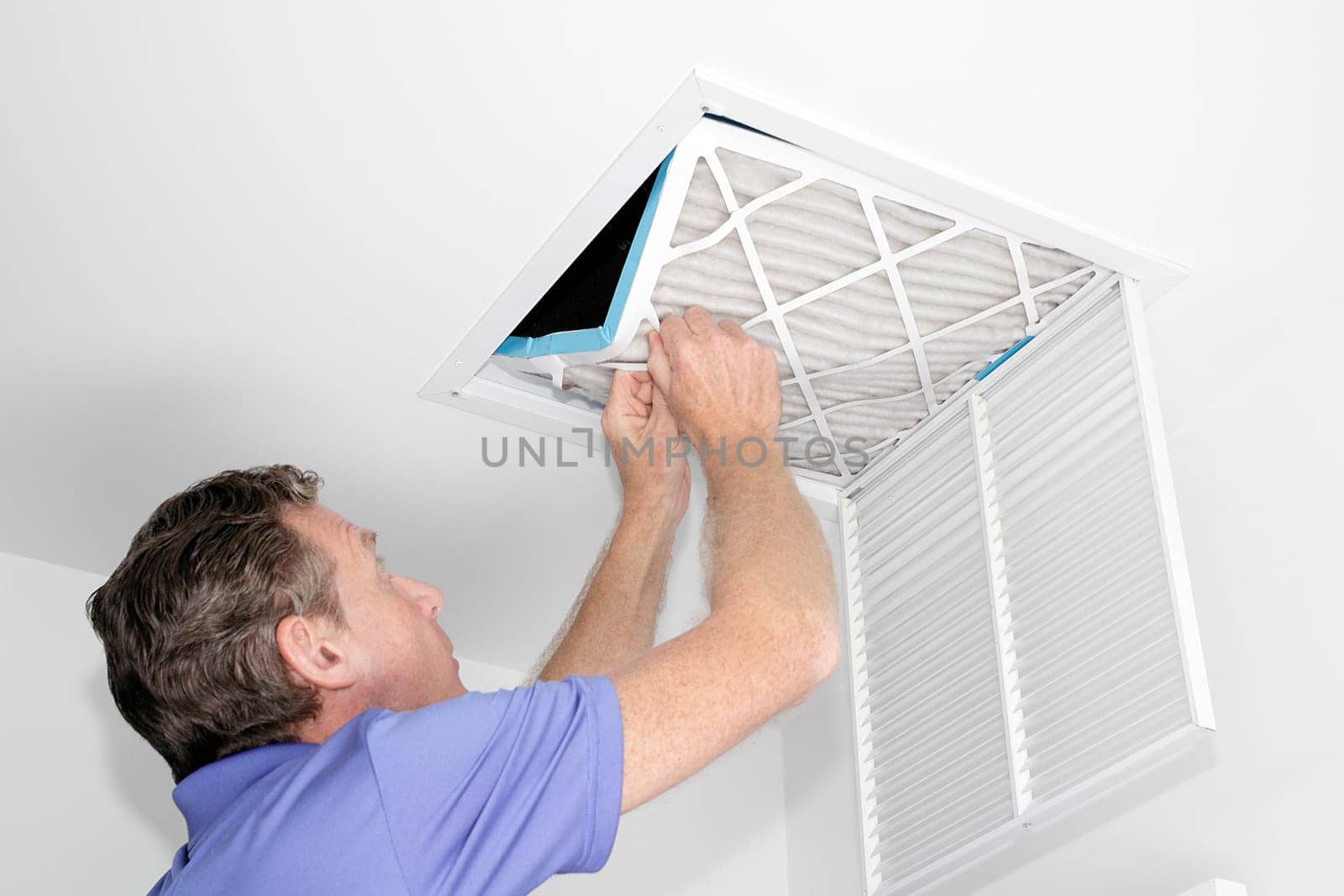 Mature man taking out a dirty air filter from a home ceiling air return vent. Male removing a dirty air filter with both hands in a house from a HVAC ceiling air vent.