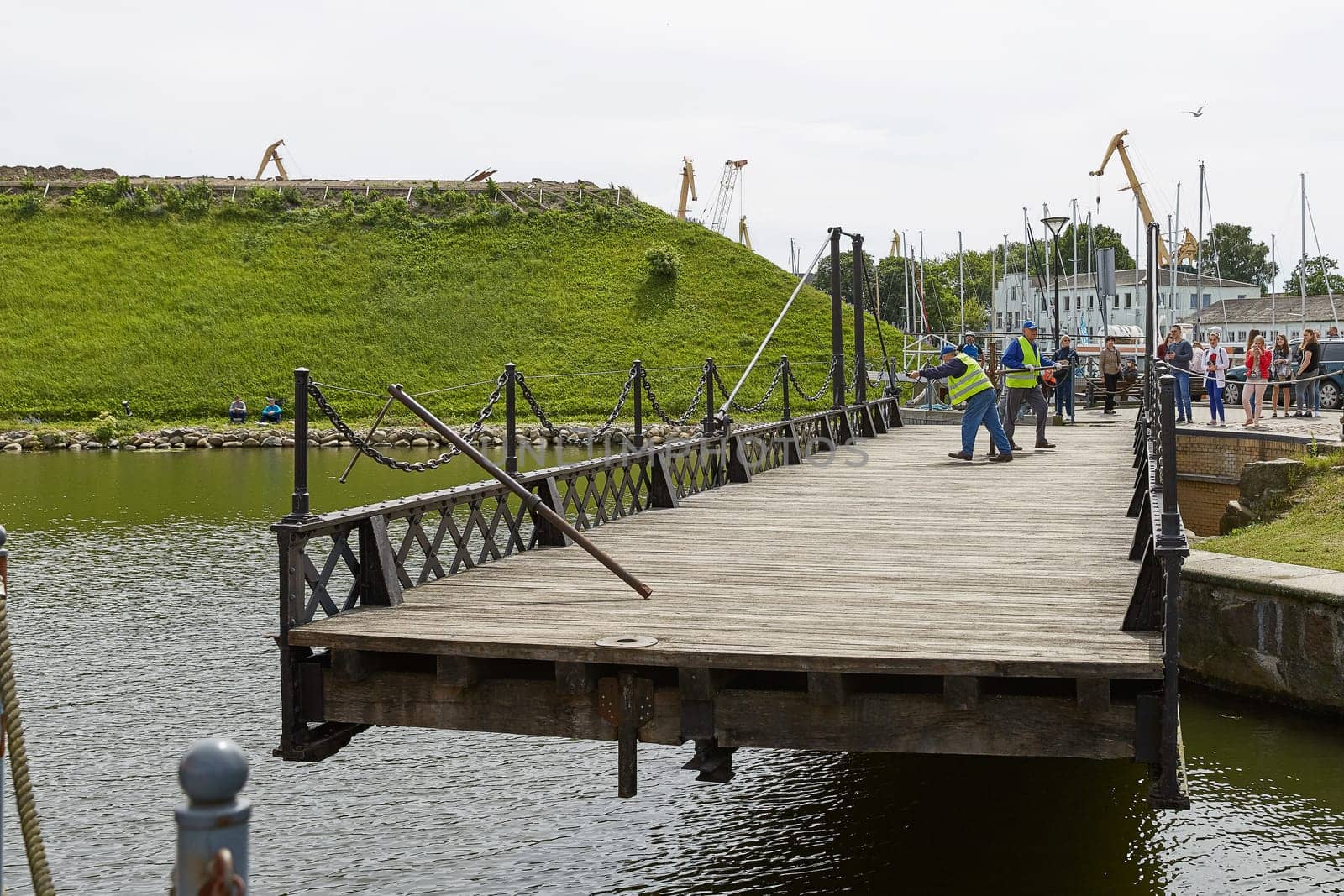 KLAIPEDA, LITHUANIA - JULY 05, 2017: Unidentified workers perform manually turn of wrought Swing bridge built in 1855 in Castle port of Klaipeda across moat Dassel between Castle Pond and river Dange. It is only mechanism of its type in Baltic countries