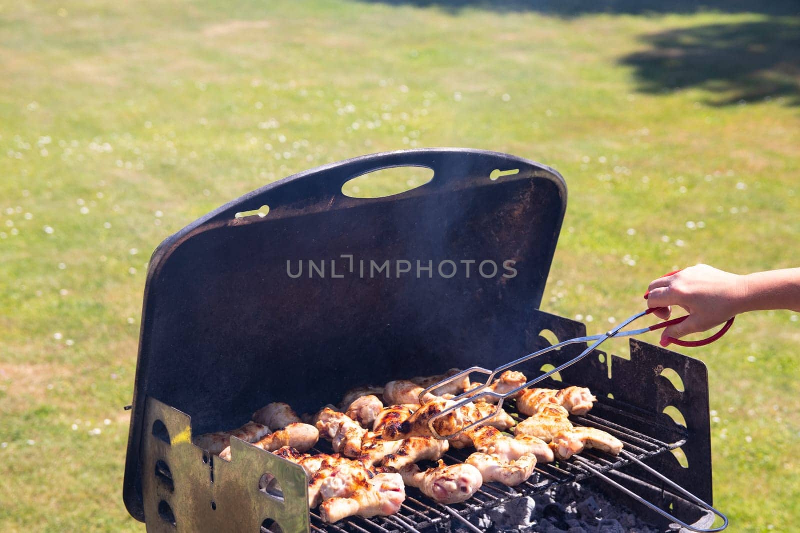 Woman is grilling chicken meat and using barbecue tongs. Concept food