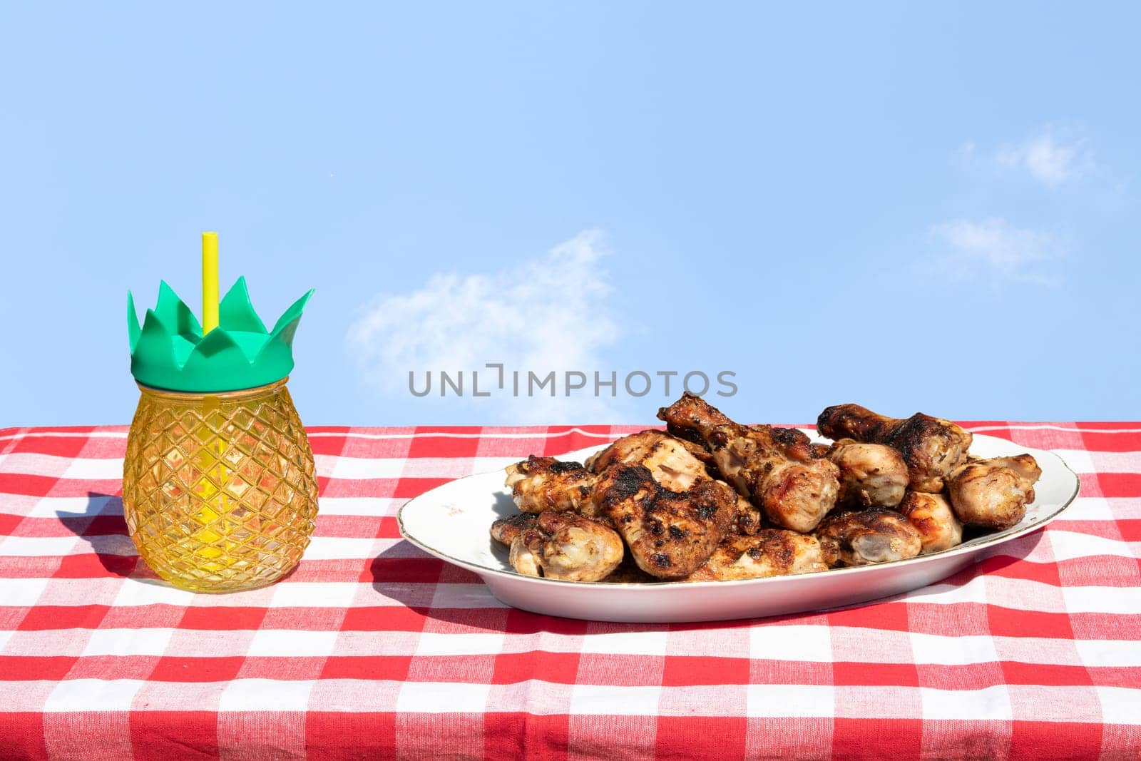 Fresh grilled chicken meat and a glass of juice on table with bright sky.