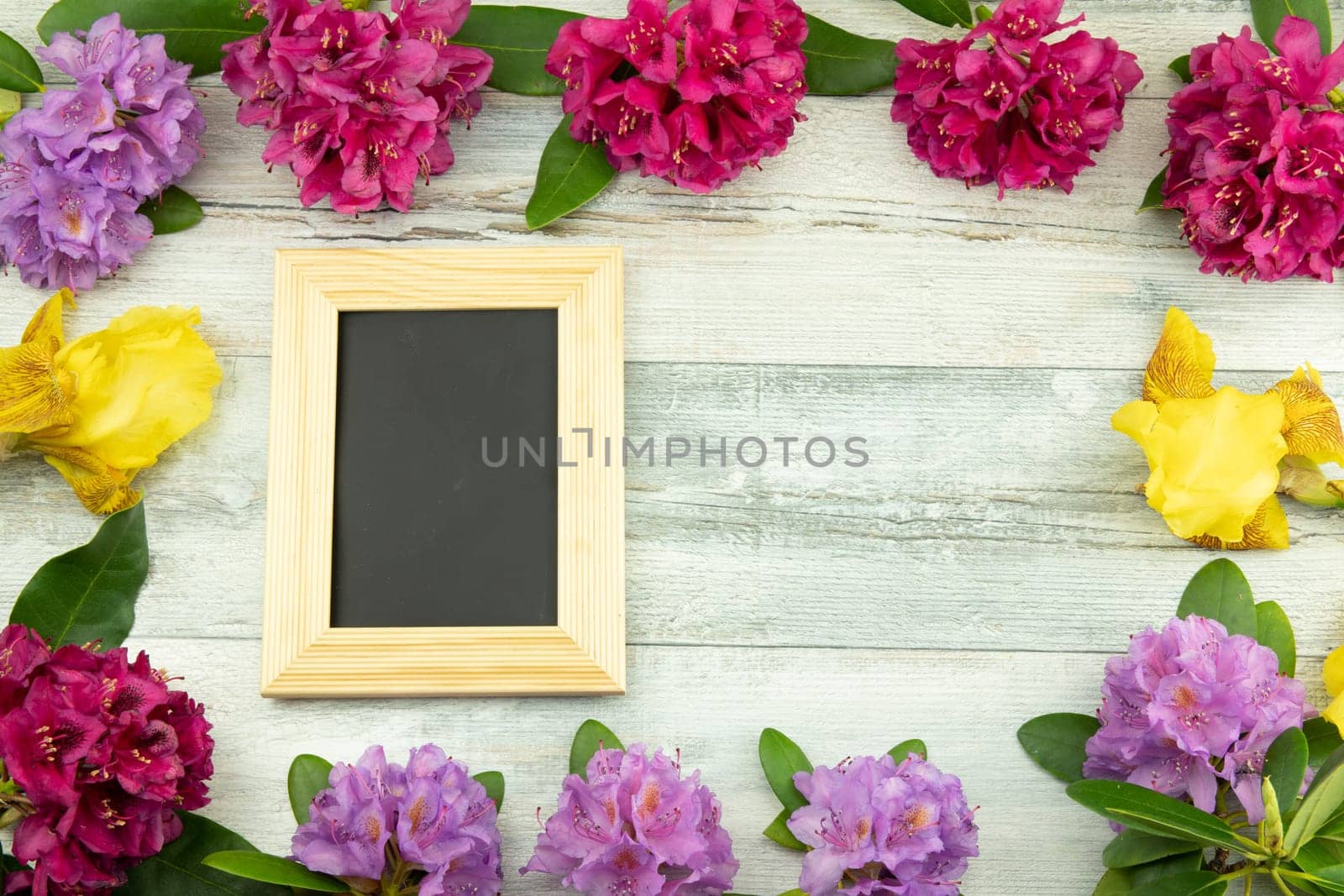 Topview from a Frame from flowers Rhododendron, Azalee and Iris on wooden table background with a blackboard for your text. Concept nature.