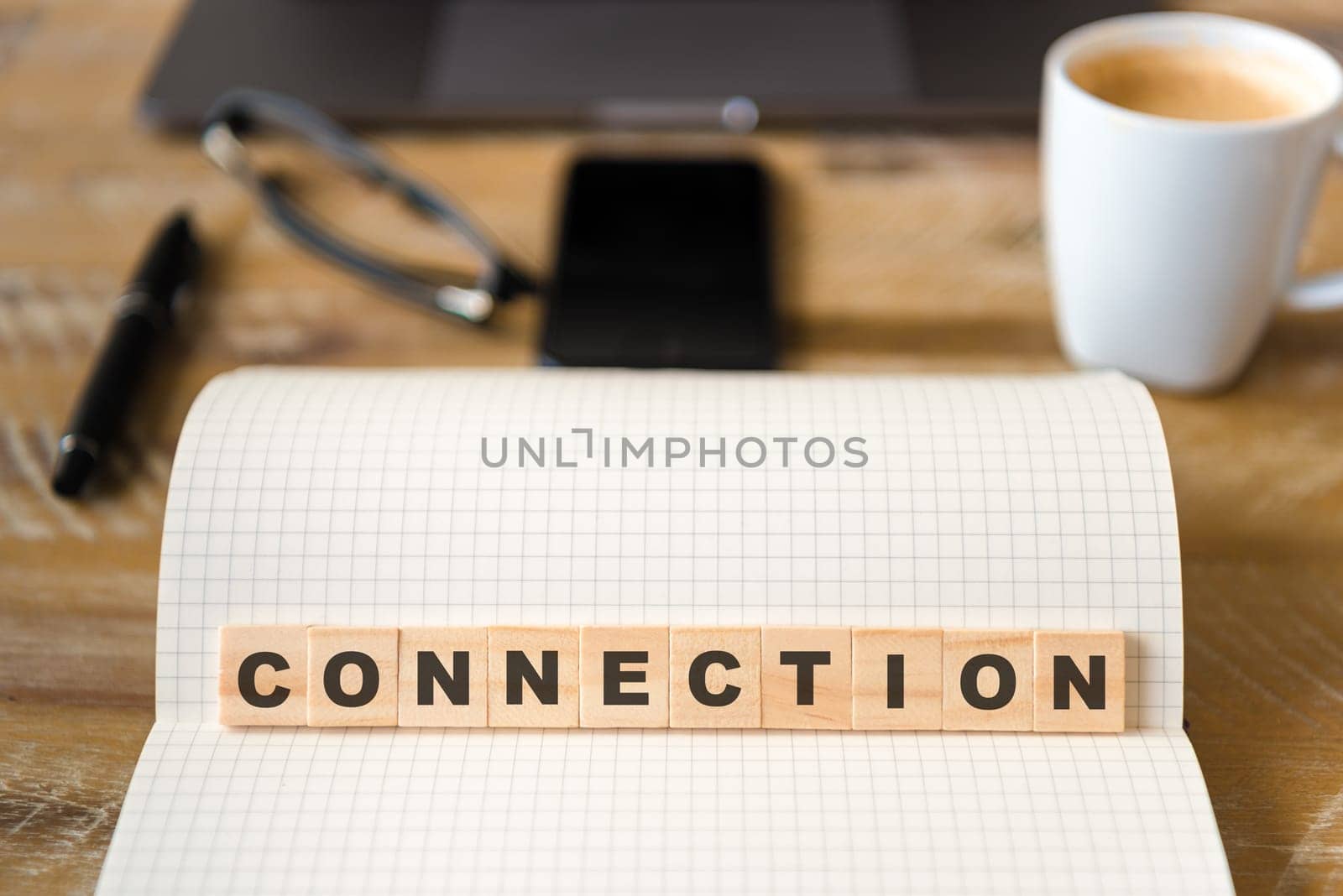 Closeup on notebook over wood table background, focus on wooden blocks with letters making CONNECTION word. Business concept image. Laptop, glasses, pen and mobile phone in defocused background