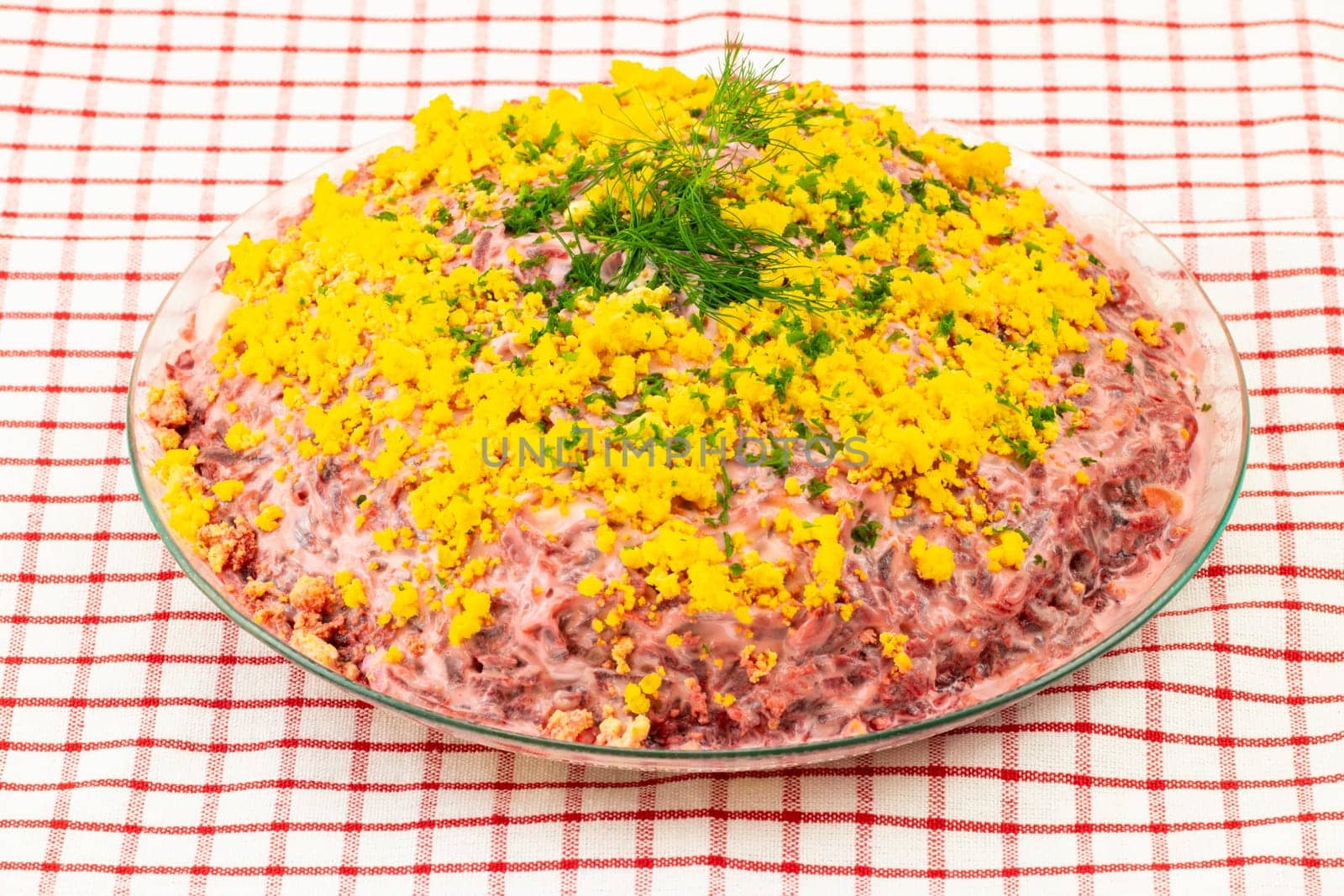 Traditional russian layered salad named herring under a fur coat. Traditional Russian cuisine presented at red checkered tablecloth. Concept Russian food.