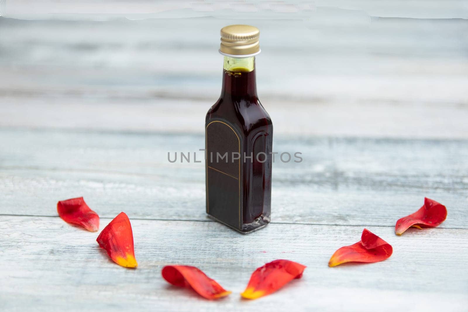 Bottle with oil and fresh tulips pedals on bright rustic wooden table with text copy space.