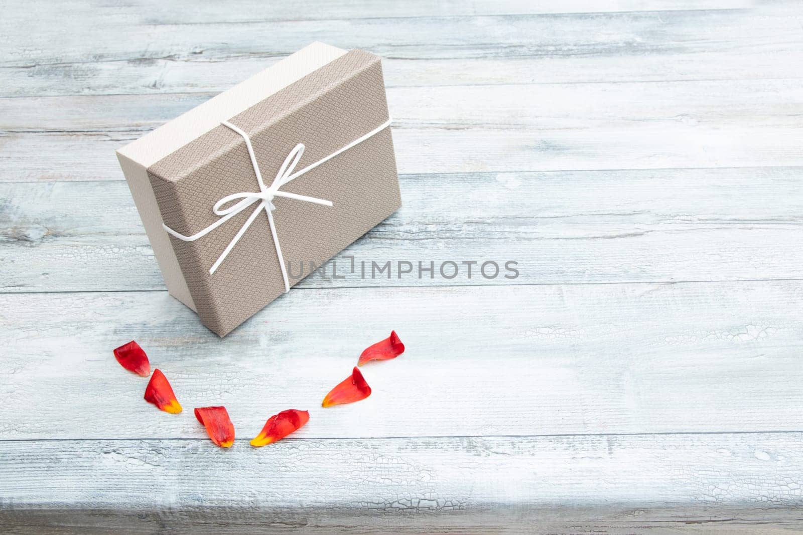 Gift box and  tulips petals with place for your text on rustic bright wooden table. Card concept.