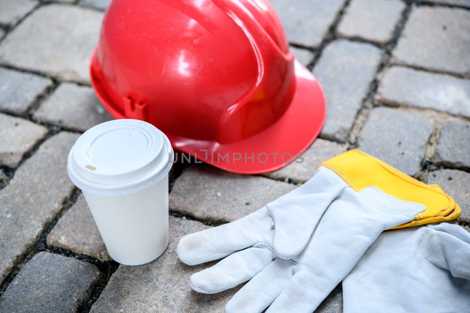 red helmet,coffee mug and work gloves on stones