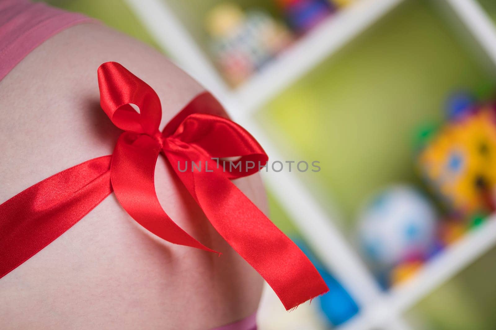 Pregnant woman belly with red ribbon gift